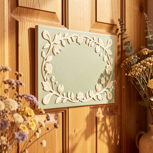 Plaque de porte décorative personnalisée, ornée de motifs botaniques, installée sur une porte en bois dans une entrée chaleureuse.